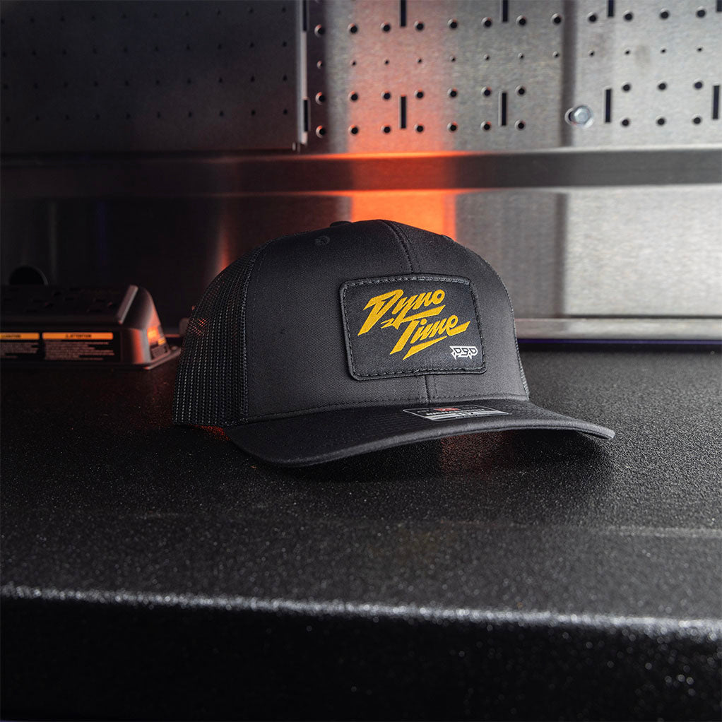 Adjustable snapback Black hat with a woven patch with gold text. 